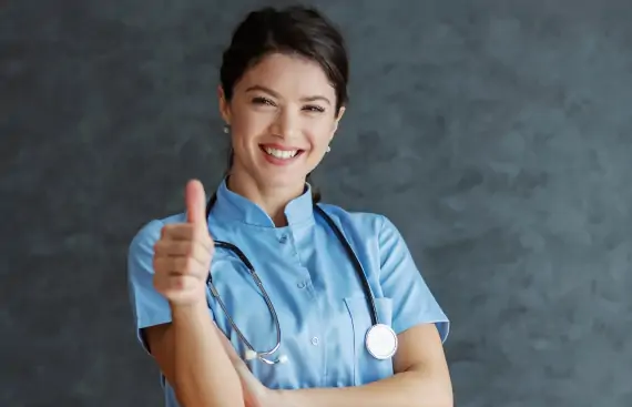 Uśmiechnięta pielęgniarka pokazuje wyciągnięty kciuk w górę